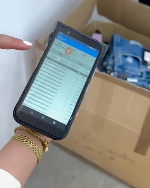 Terminal RFID portable tenu devant un carton fermé, la liste des articles lus à l'écran.